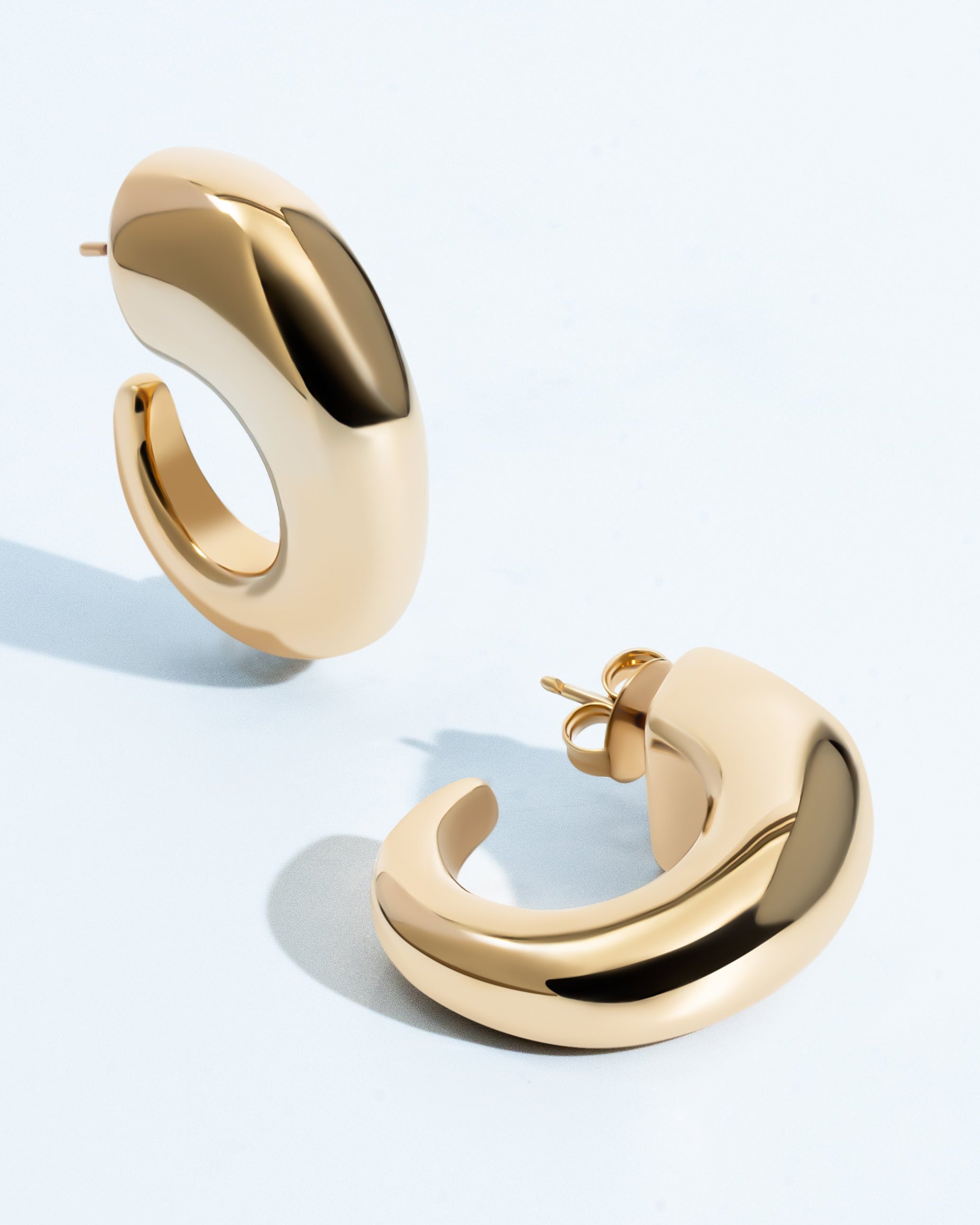 Oval open hoop earrings available in gold plated and rhodium plated finishes with sculptural thick design