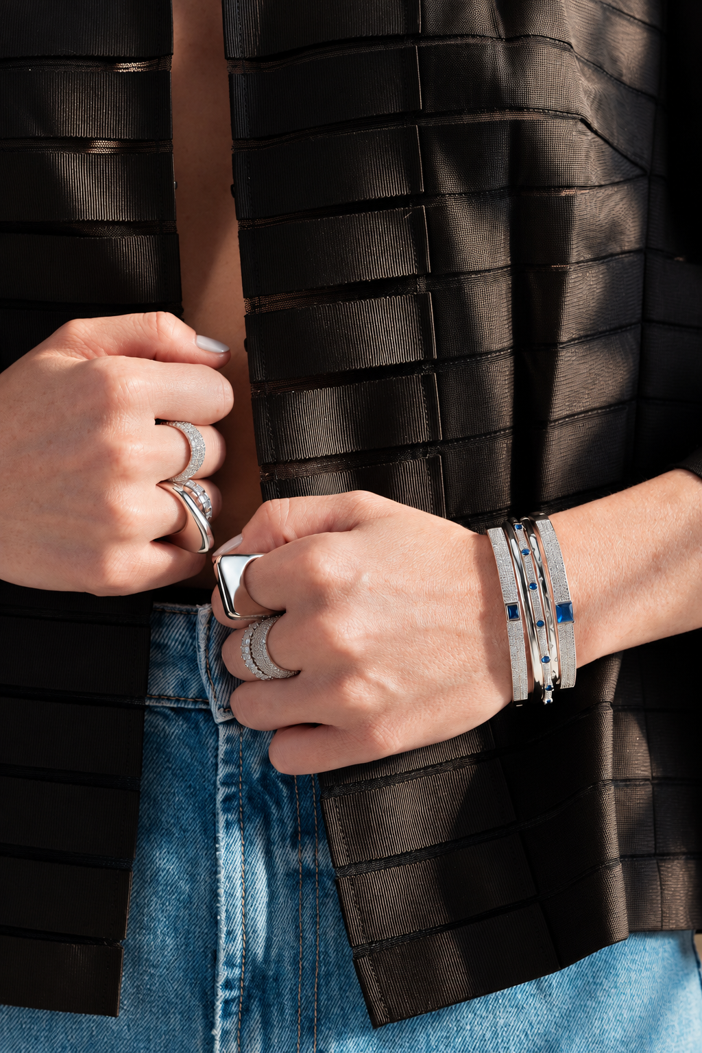Lifestyle photo of a woman with her hand near her face against a dark background, styled with a bangle bracelet layered together with a necklace, or stacked with rings.