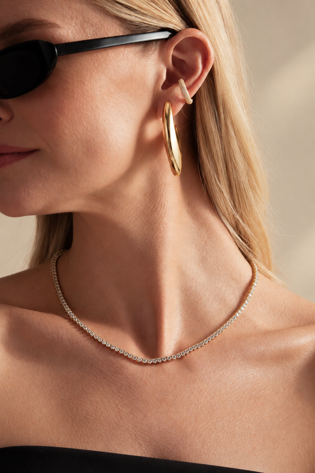 Lifestyle close-up of a woman in sunglasses wearing a necklace, styled together with a gold pave ear cuff and a gold sail-shaped drop earring.