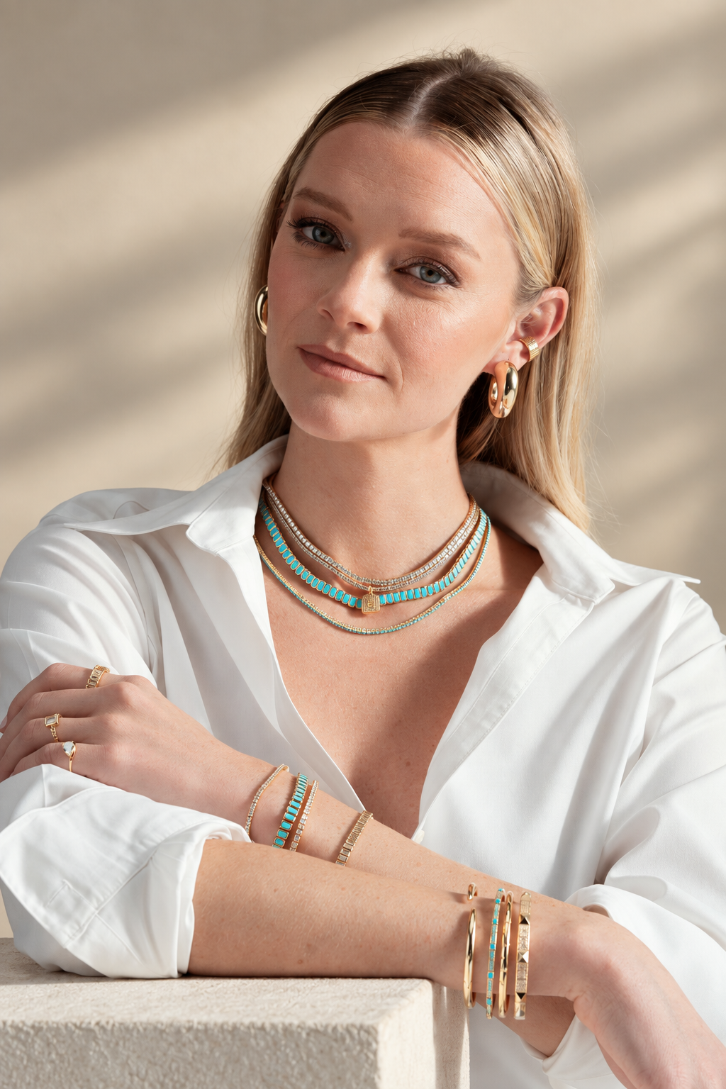 Lifestyle photo of a woman in a white shirt leaning on a table, styled with a chunky pave ear cuff, bracelets, and a pendant necklace worn together.