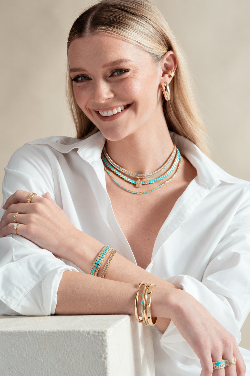 Lifestyle photo of a woman in a white shirt leaning on a table, wearing the chunky pave ear cuff along with bracelets, from a different angle.