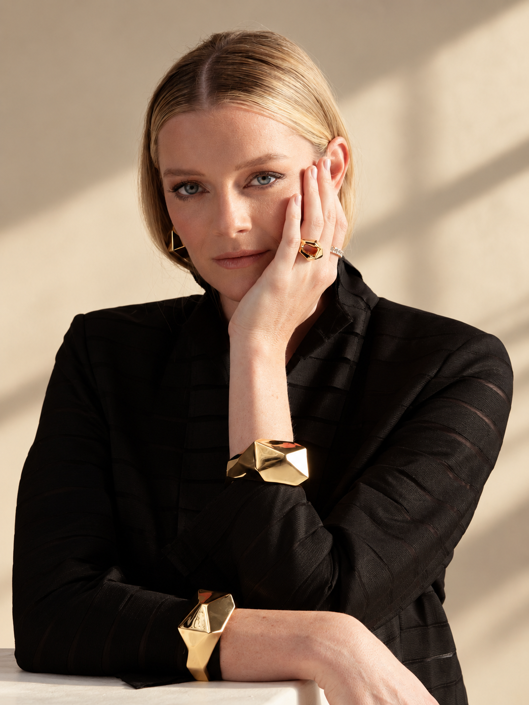 Lifestyle photo of a woman in a black top resting her head on her hand, wearing the geometric faceted ring and a bracelet.