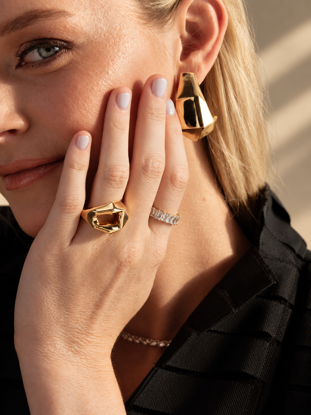 Lifestyle close-up of a woman in a black top with her hand near her face, wearing the geometric faceted ring and an earring.
