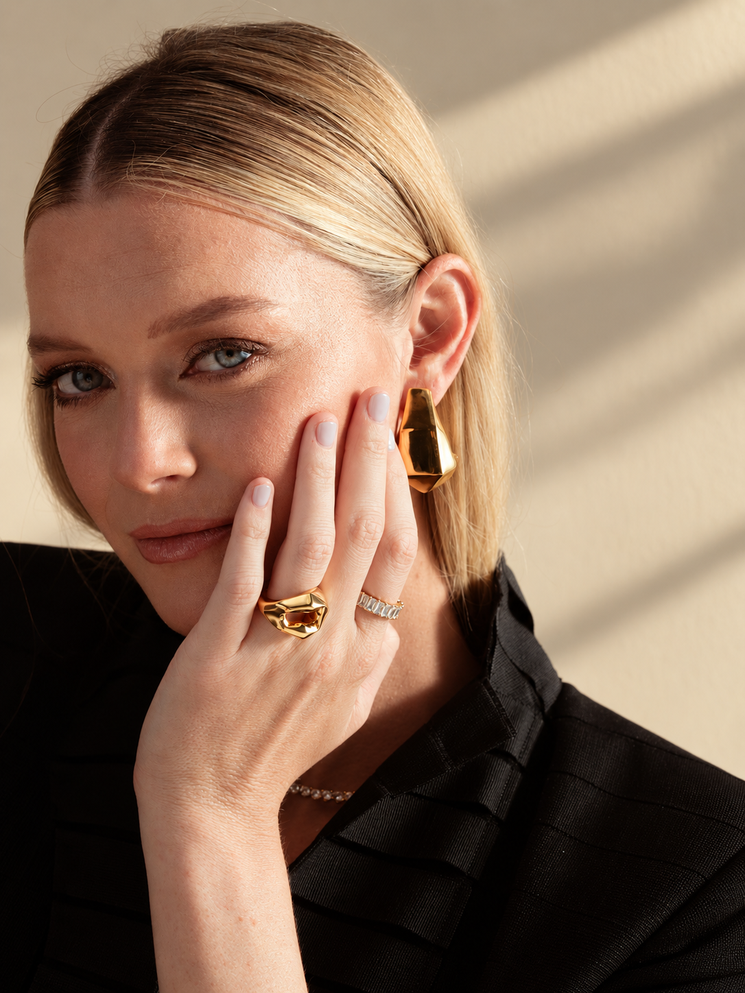 Lifestyle close-up of a woman in a black top with her hand near her face, wearing the geometric faceted ring and an earring, from another angle.