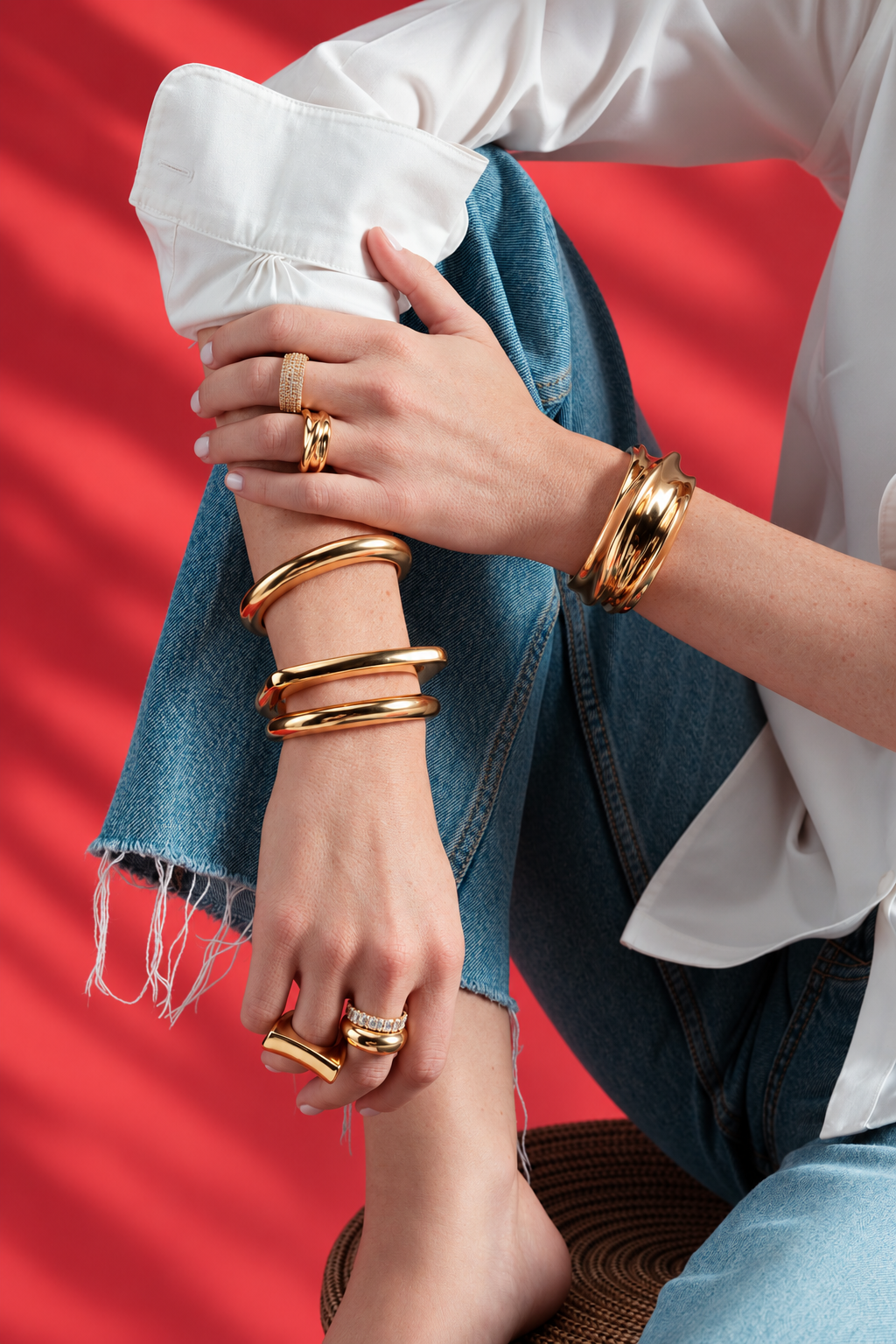 Lifestyle photo of crossed wrists against a red background, wearing stacked gold bangles and rings along with the chunky sculptural ring, with a white sleeve.