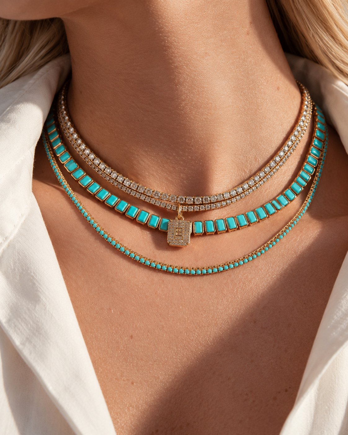 Lifestyle close-up of a woman's chest wearing a layered teal beaded necklace along with the initial letter pendant necklace.