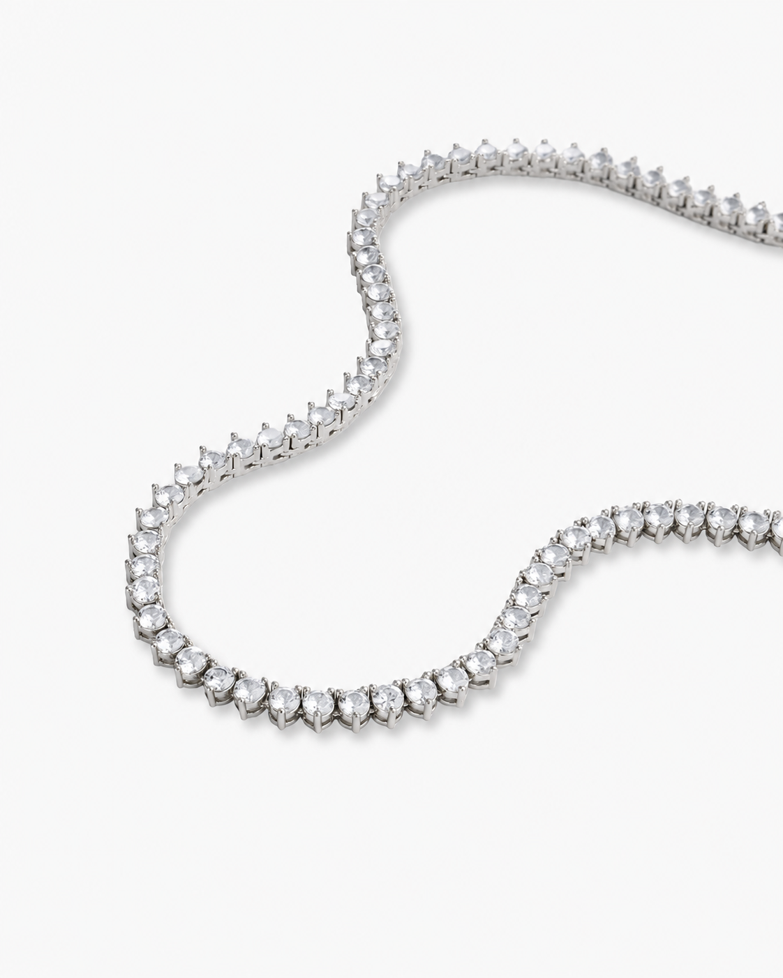 Silver three-prong tennis necklace with simulated diamond stones, alone product shot laid in a curved squiggle shape.