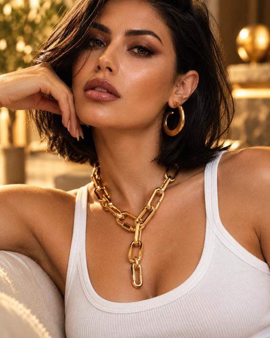 Close-up of a woman resting her chin on her hand, wearing the Antonia gold paperclip chain choker necklace and gold hoop earrings, warm lighting
