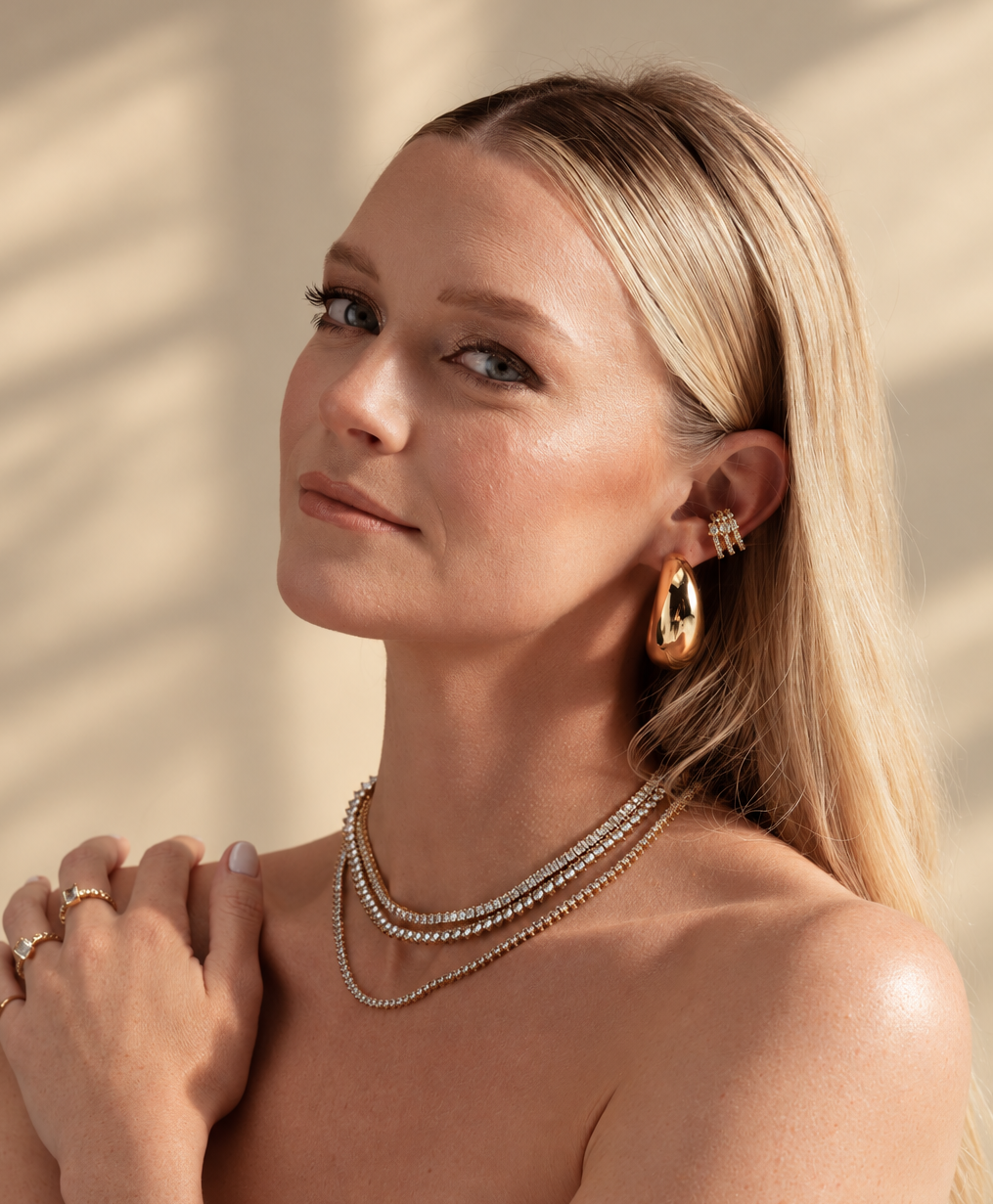 Lifestyle photo of a woman with her hand near her chest, wearing the chunky geometric ear cuff along with layered necklaces.
