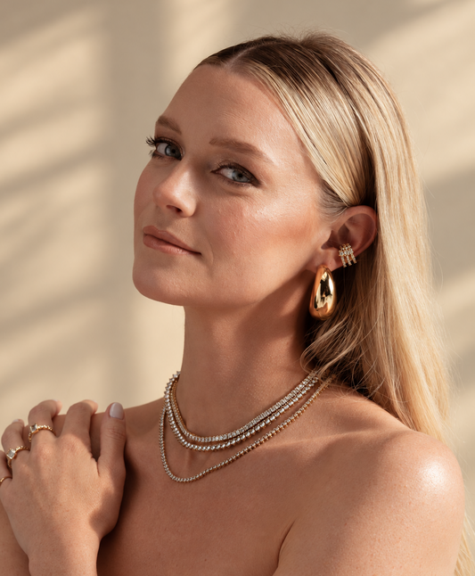 Lifestyle photo of a woman with her hand near her chest, wearing the chunky geometric ear cuff along with layered necklaces.