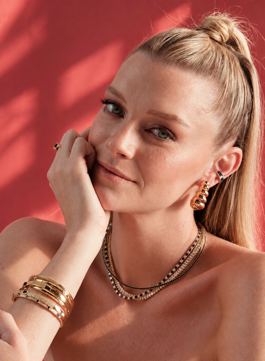 Lifestyle photo of a woman against a red background with her hand near her chin, wearing the multicolor tennis necklace.