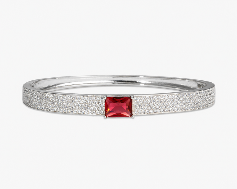 Gold pave bangle bracelet with a single red simulated diamond stone, alone product shot on a plain background.