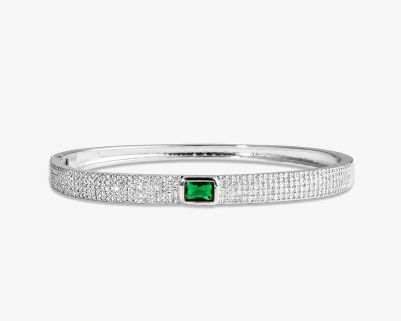 Silver textured bangle bracelet with a green simulated diamond accent stone, alone product shot on a plain background.