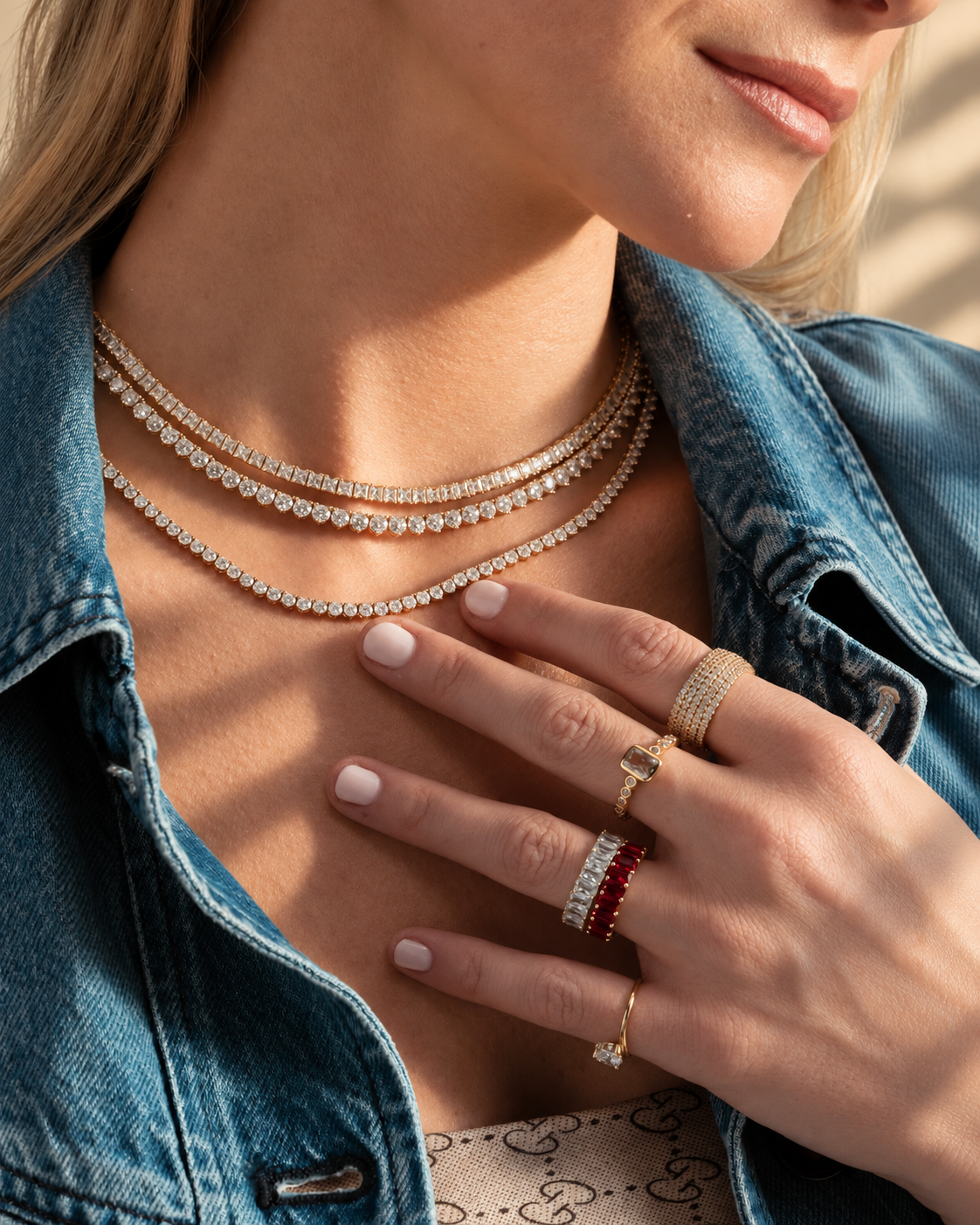Lifestyle close-up of a woman's neckline in a denim jacket with her hand near her chest, styled with a ring and layered necklaces worn together.