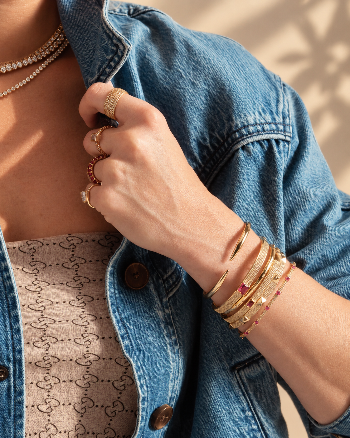 Lifestyle close-up of a hand adjusting a denim jacket collar, styled with multiple bangle bracelets stacked together with red and pink beaded accents.