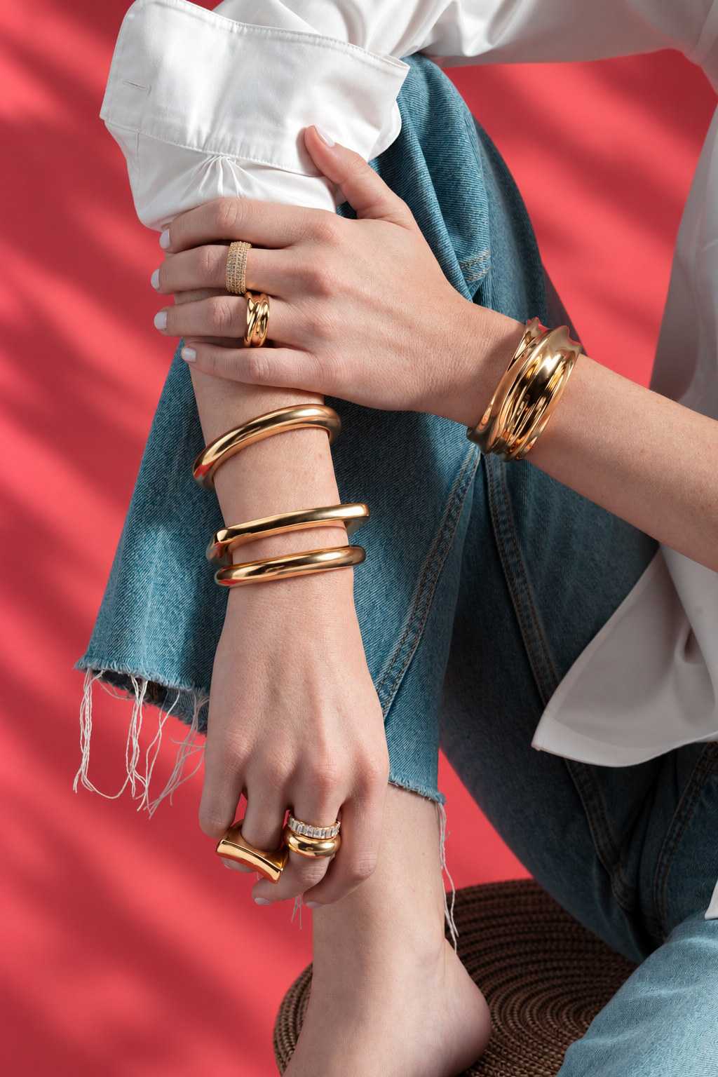 Close-up of a wrist stacked with gold bangles, wearing the Caroline gold statement ring, red background