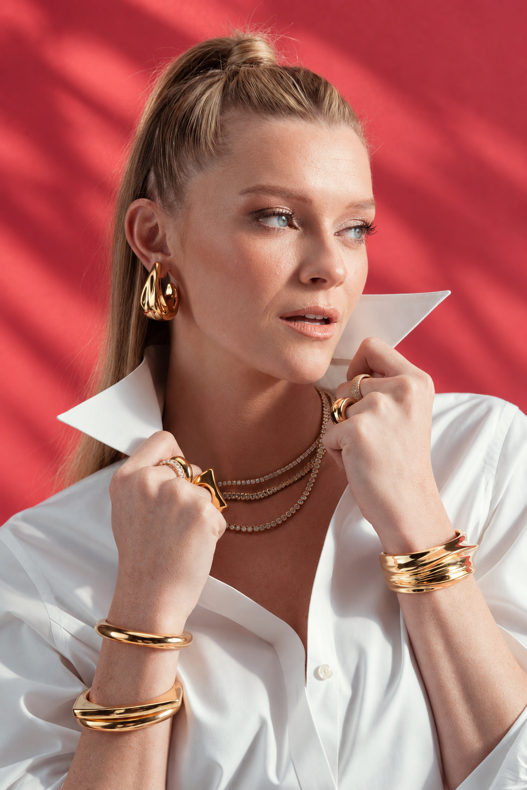 Woman adjusting her collar, wearing a necklace and the Sophia silver cuff bracelet stacked with gold bangles, red background