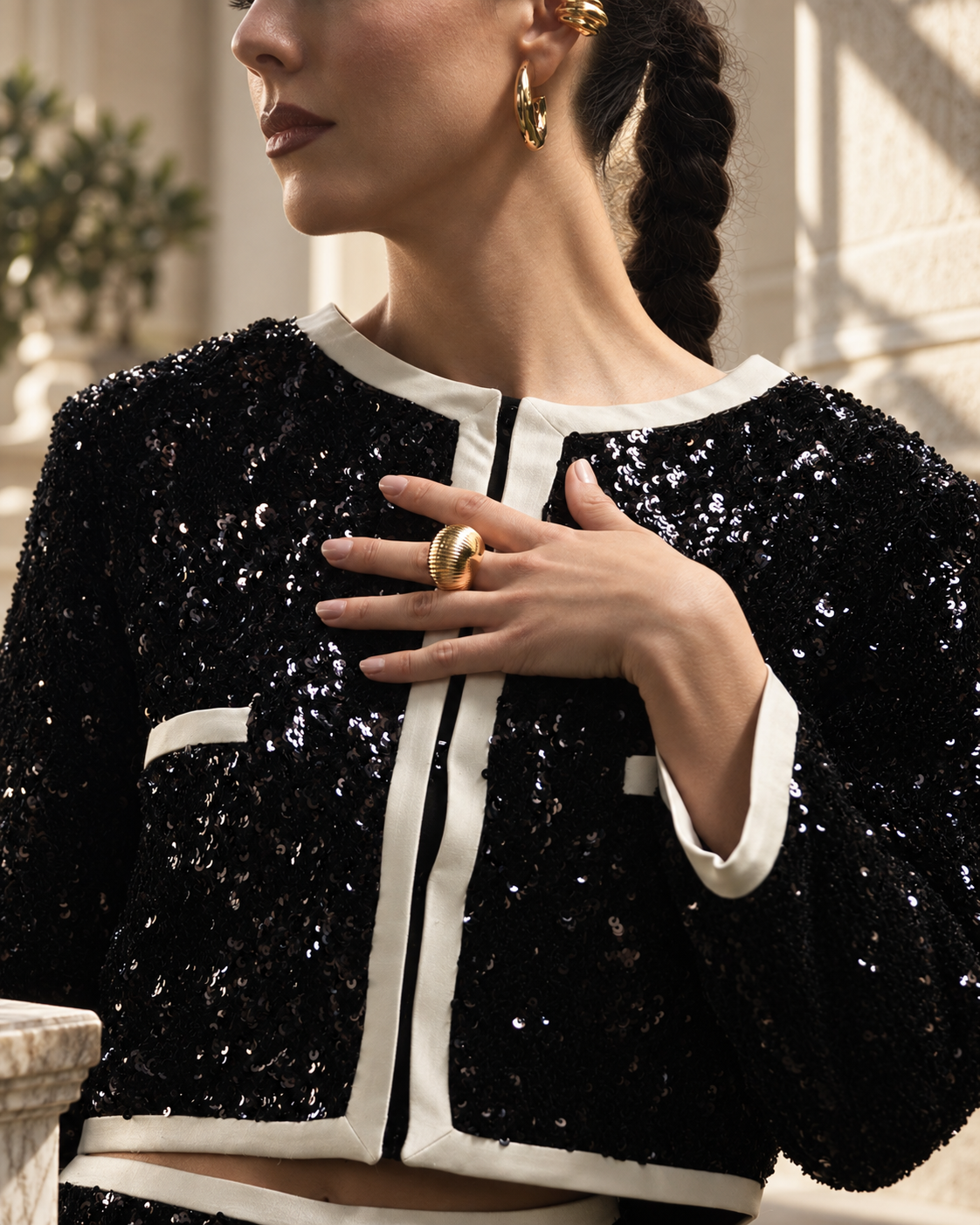 Close-up of a hand wearing the Georgia gold ribbed dome ring, black and white tweed jacket