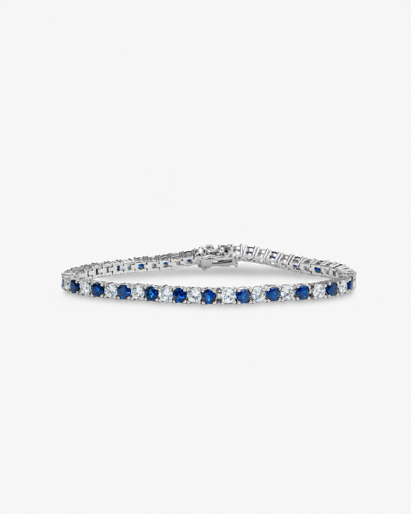 Silver tennis bracelet with blue colored stone detailing, alone product shot on a plain background.