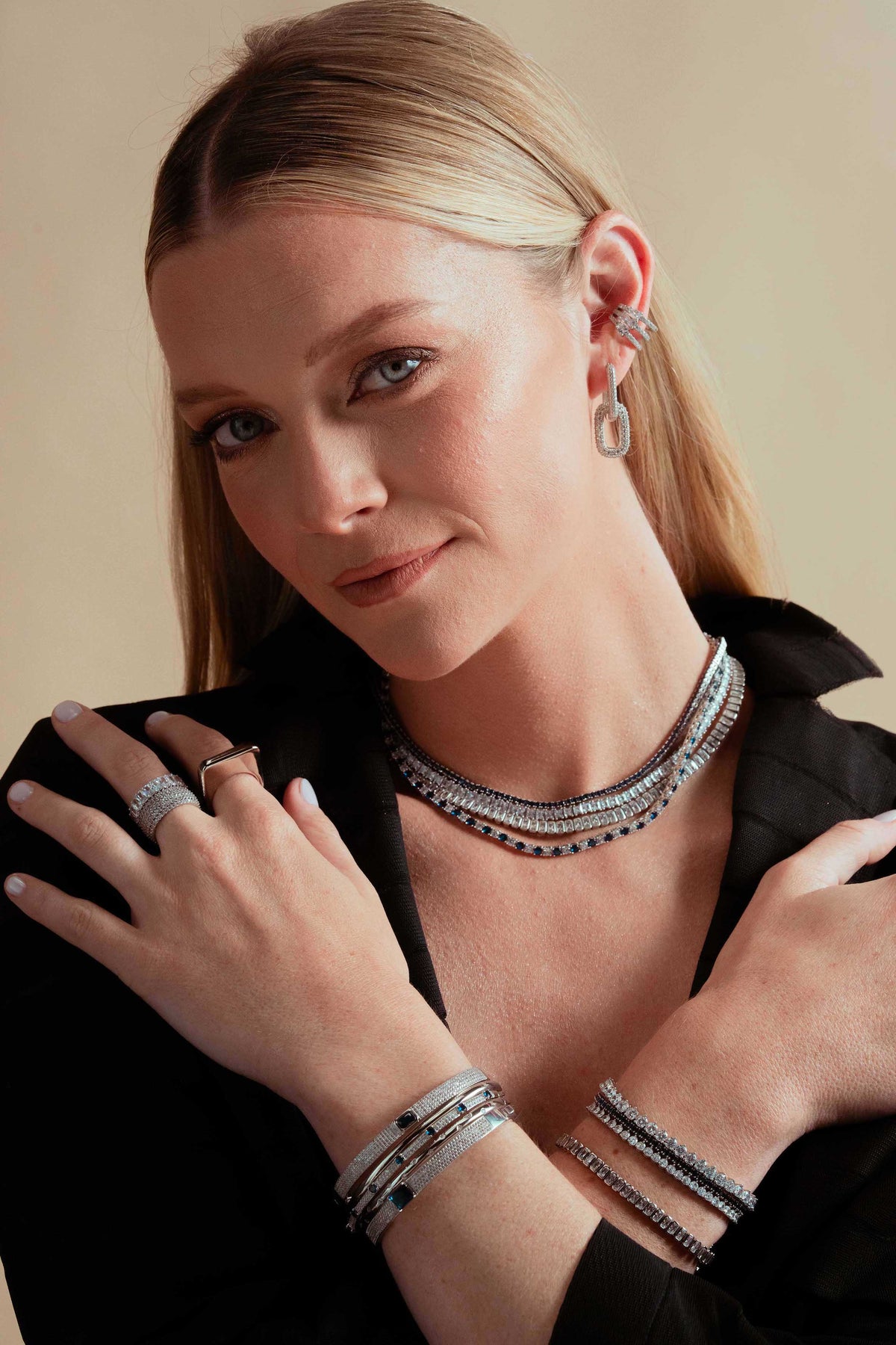 Woman with her hand near her chest wearing layered silver necklaces and the Laura silver tennis bracelet, cream background