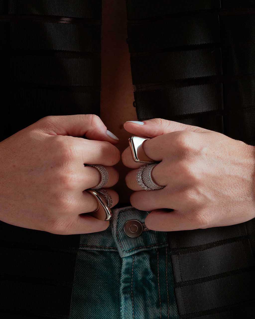 Close-up of two hands resting near a waistband, wearing the Lily silver signet ring, dark denim