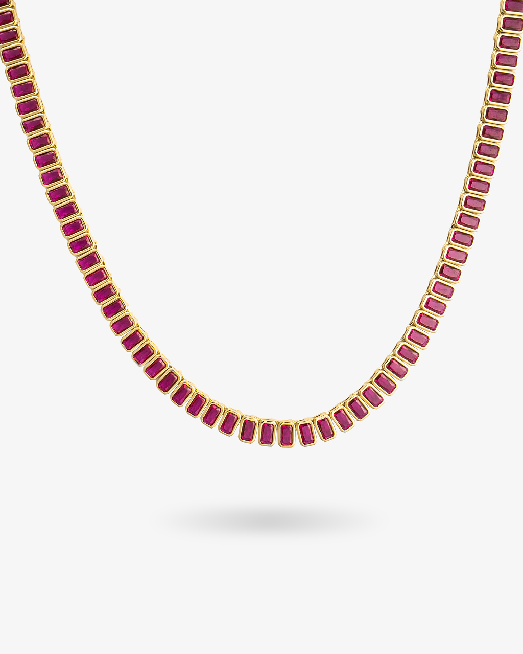 Gold tennis necklace with red baguette-cut simulated diamond stones, alone product shot on a plain background.