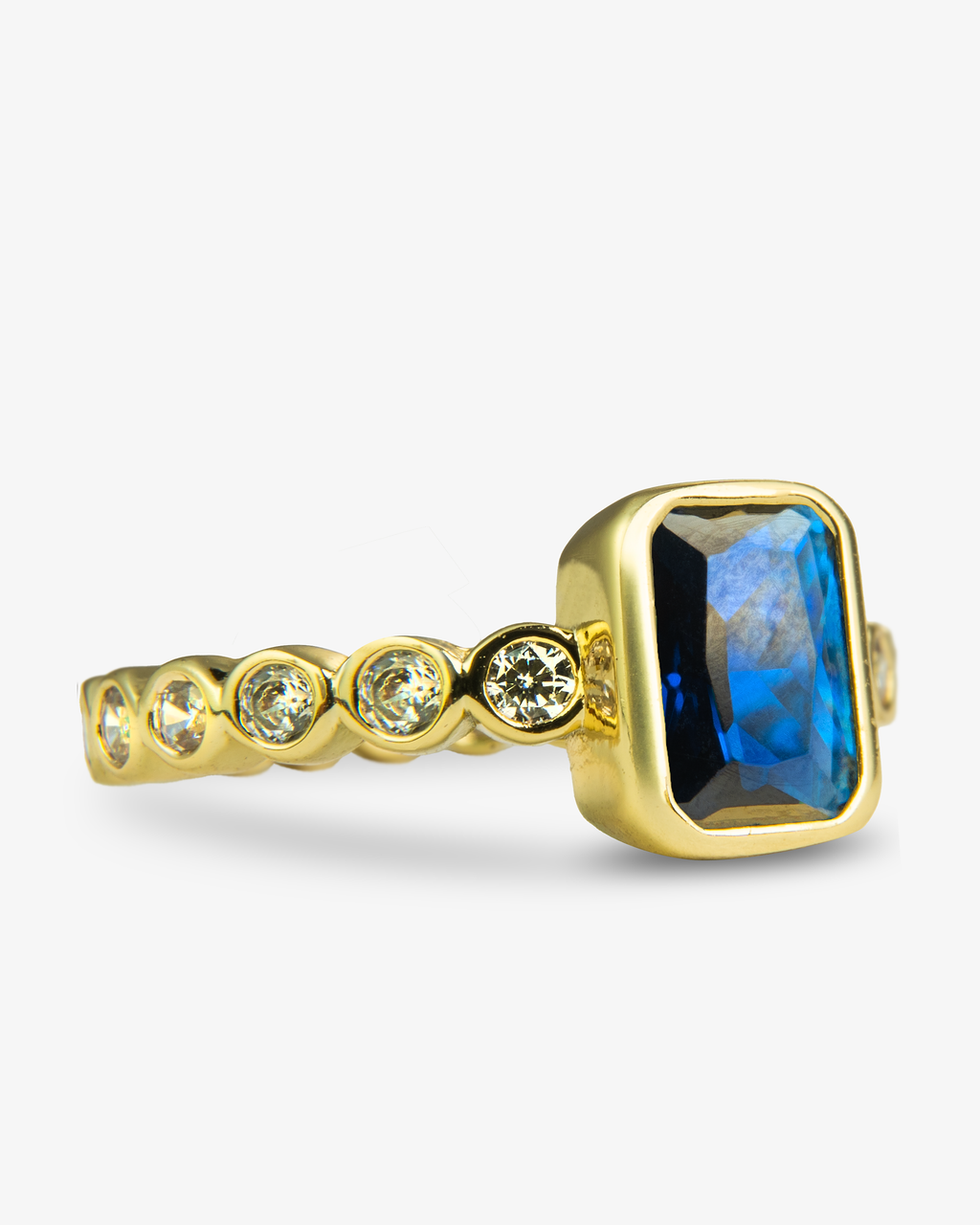 Gold ring with a blue emerald-cut simulated diamond center stone and pave band, alone close-up product shot from a different angle.