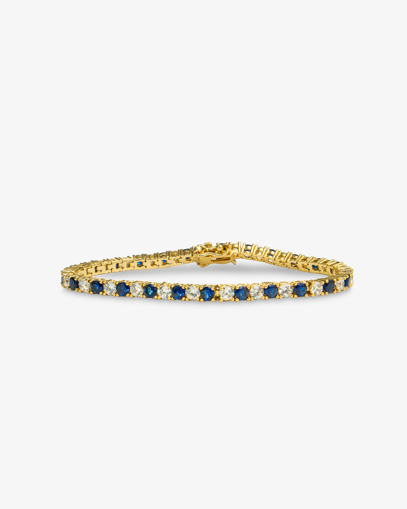 Gold tennis bracelet with blue colored stone detailing, alone product shot on a plain background.