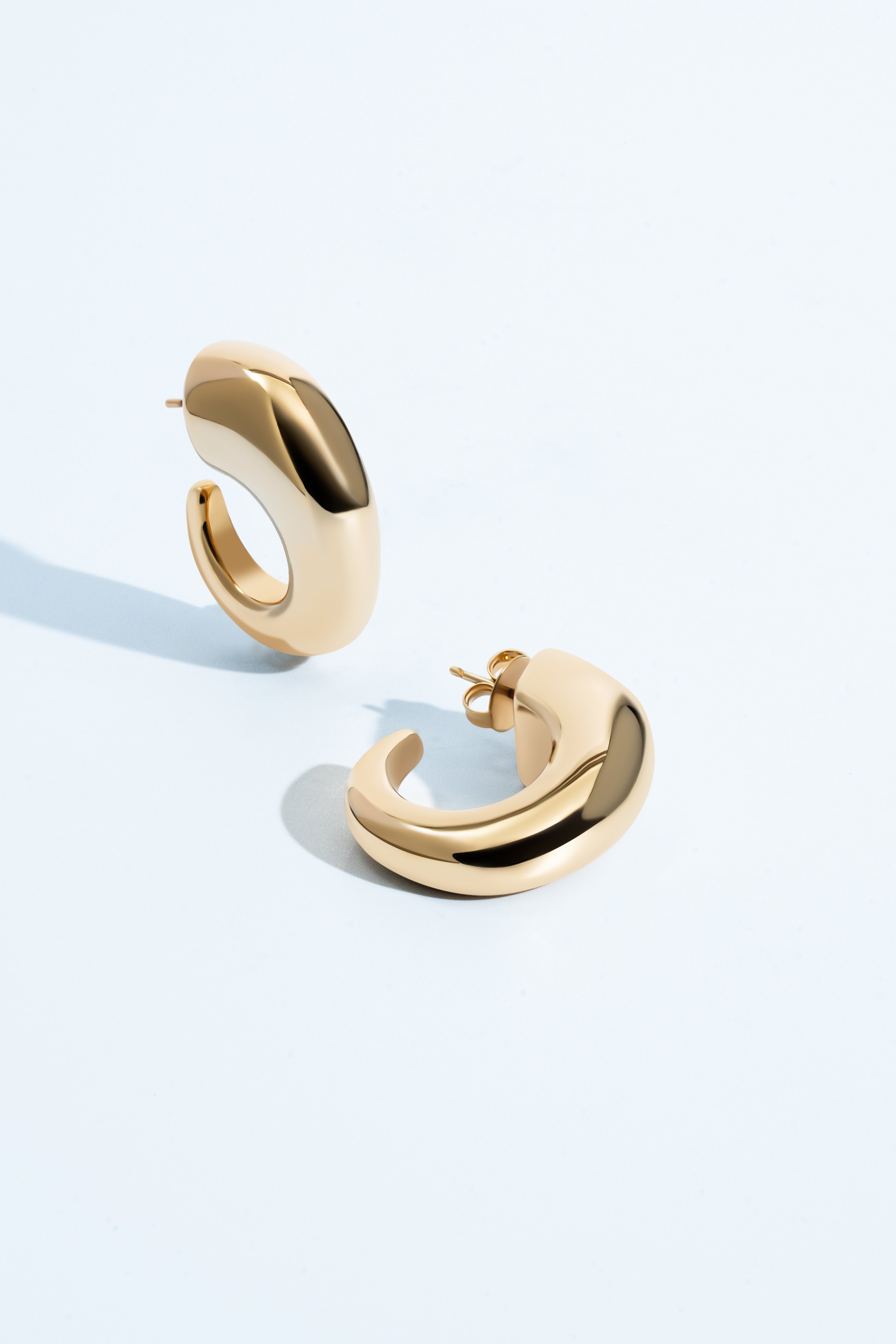 Oval open hoop earrings available in gold plated and rhodium plated finishes with sculptural thick design