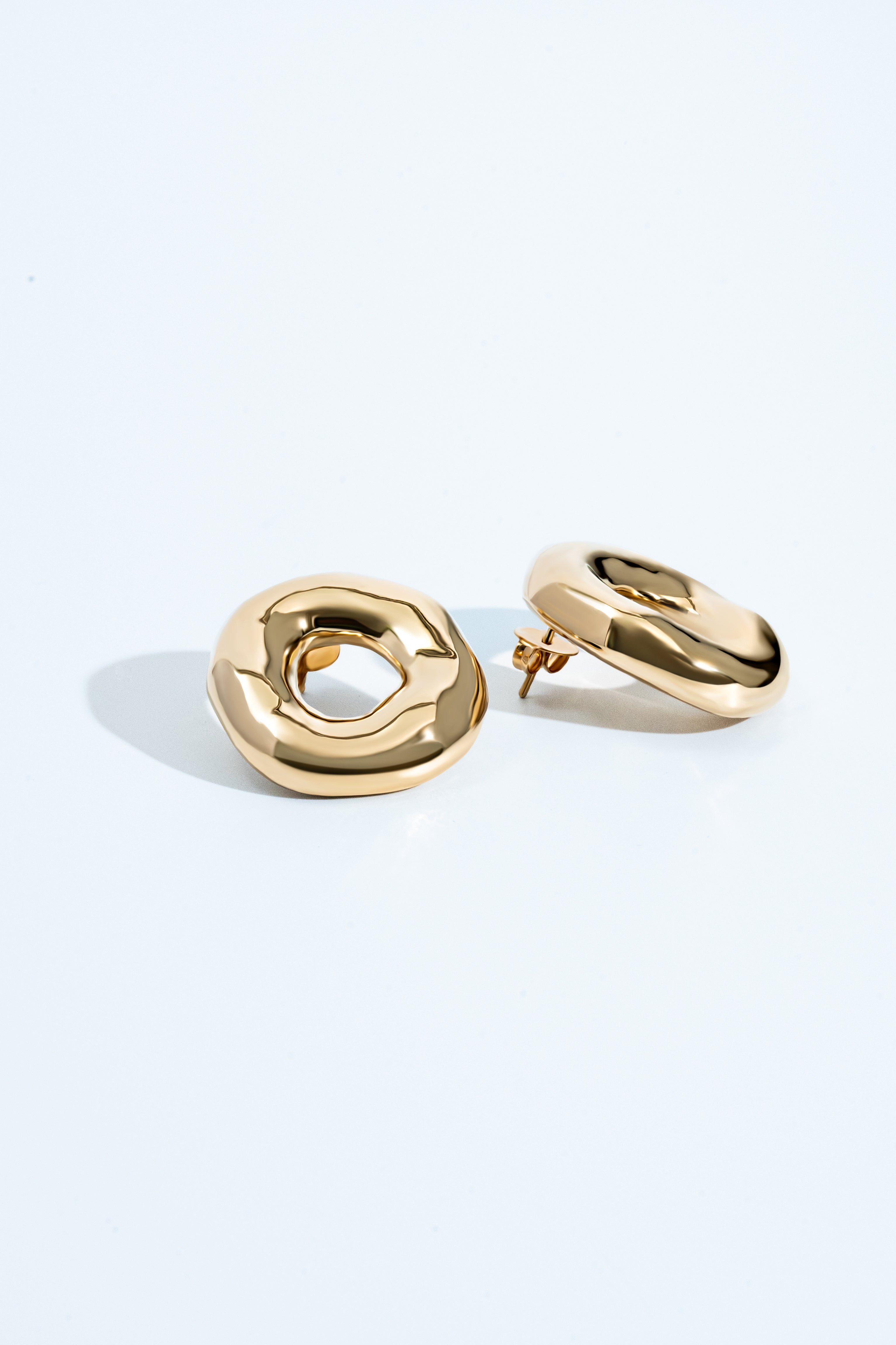 Melted circle earrings available in gold plated and rhodium plated finishes with sculptural curved design