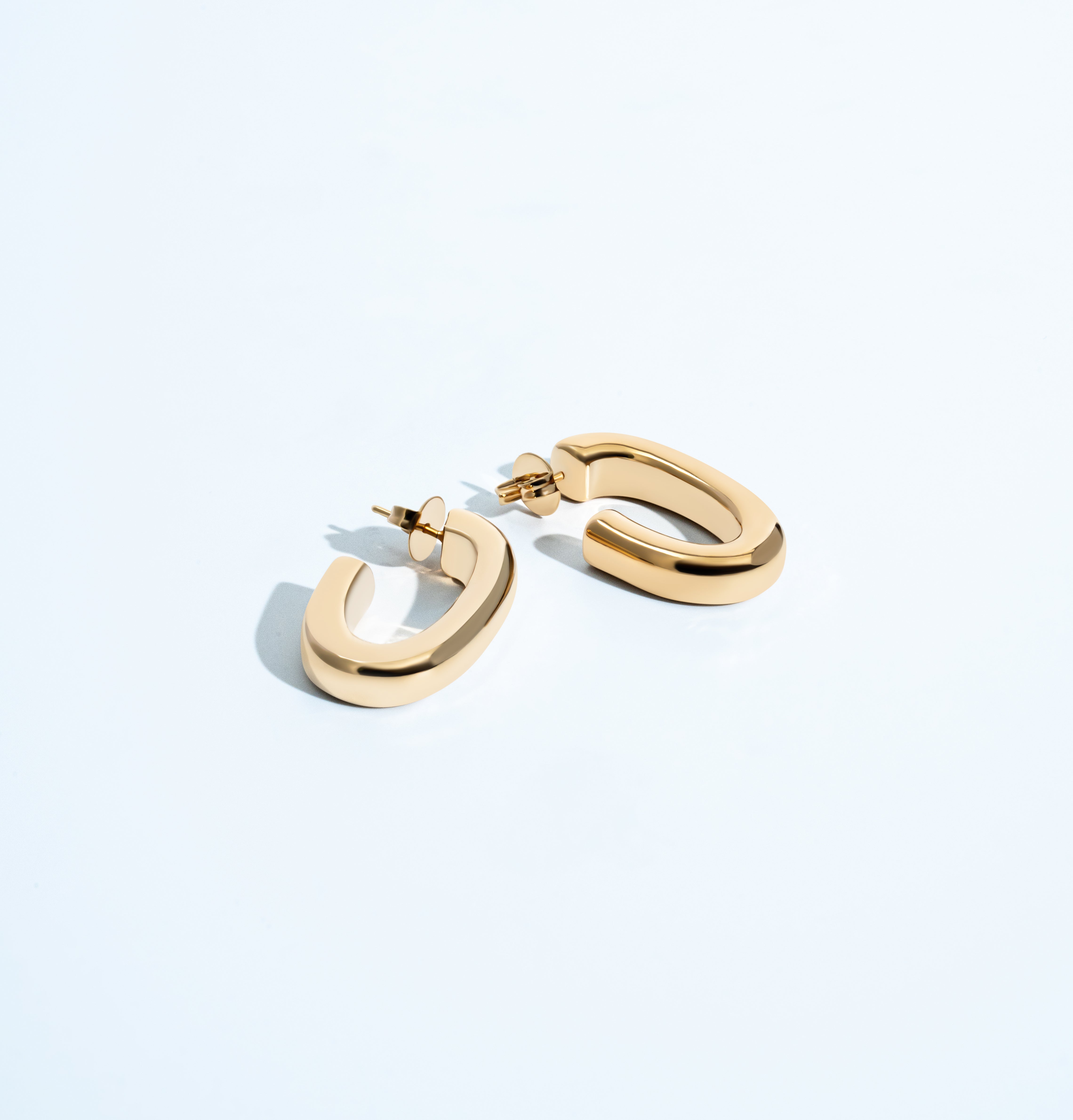 Oval open hoop earrings available in gold plated and rhodium plated finishes with sculptural curved design