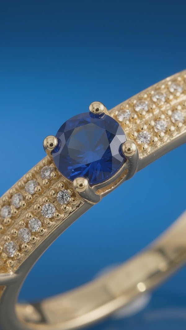 Close-up video of a gold-tone bangle bracelet featuring a central simulated blue sapphire surrounded by rows of simulated diamonds against a blue background.